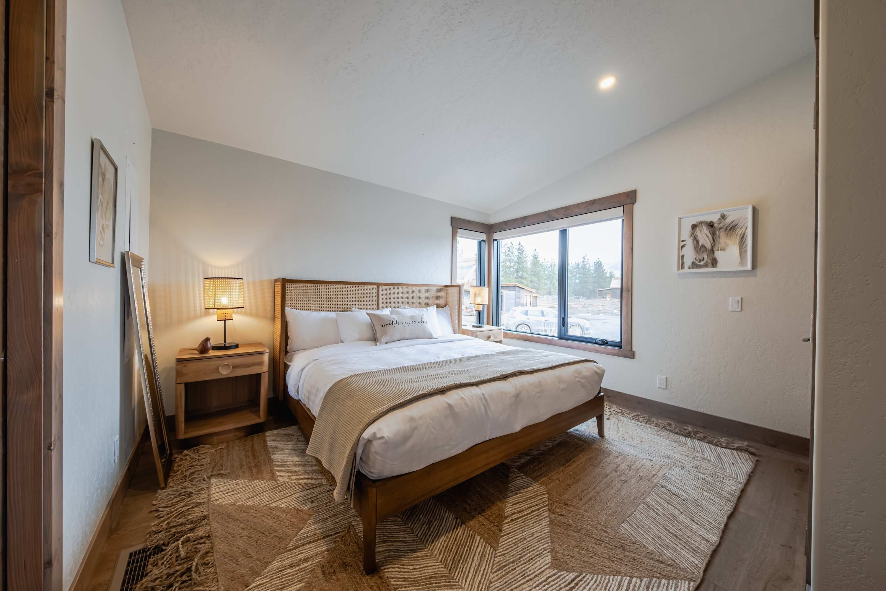 A bedroom with a wooden bed, a nightstand, a lamp, and a large window.