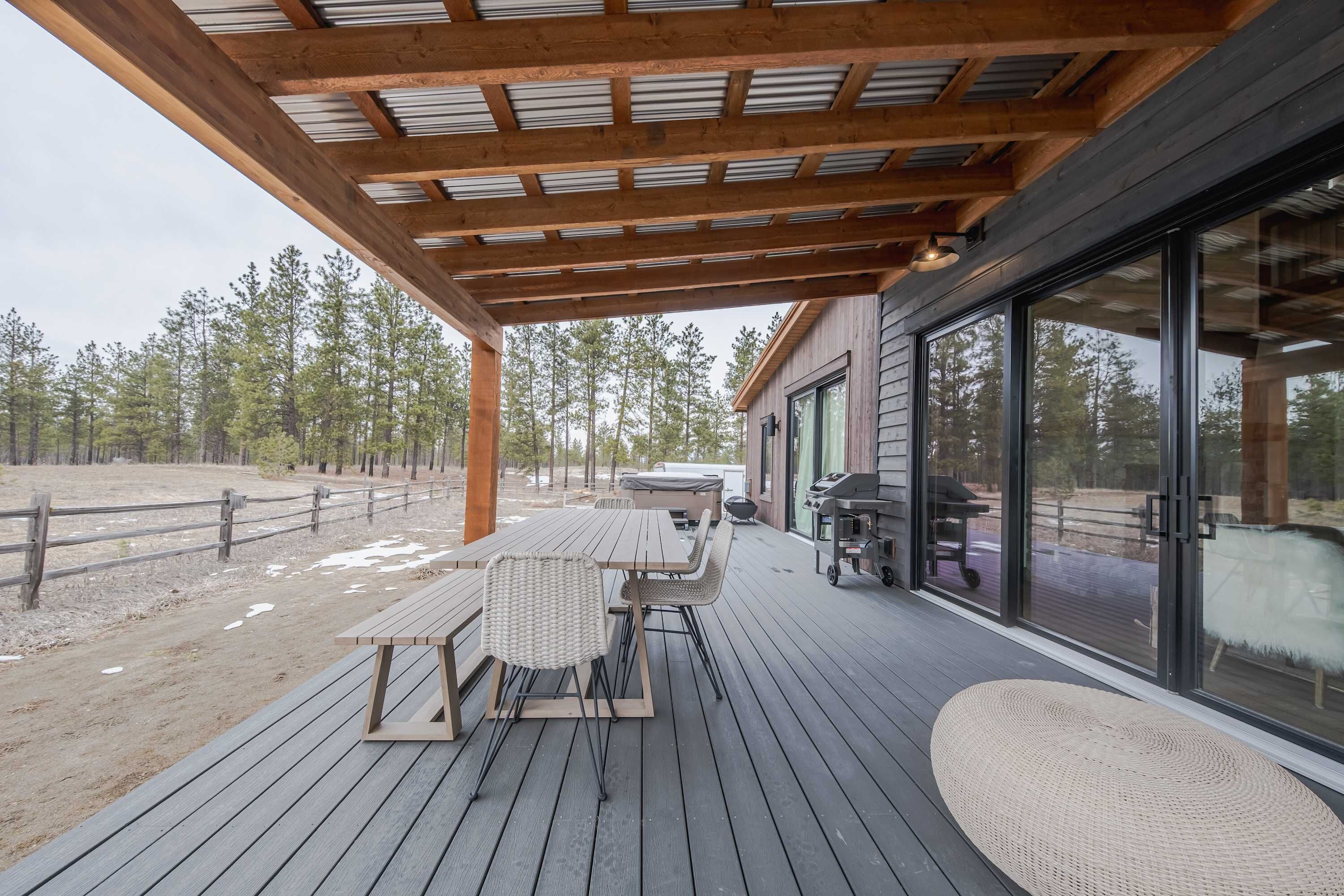 Une terrasse extérieure dotée d’une pergola en bois, d’une table avec des chaises et d’un espace barbecue.