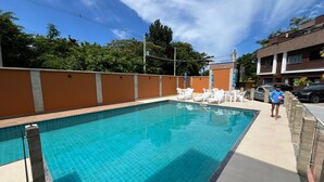 Una piscina con sillas reclinables blancas y un borde de baldosas.