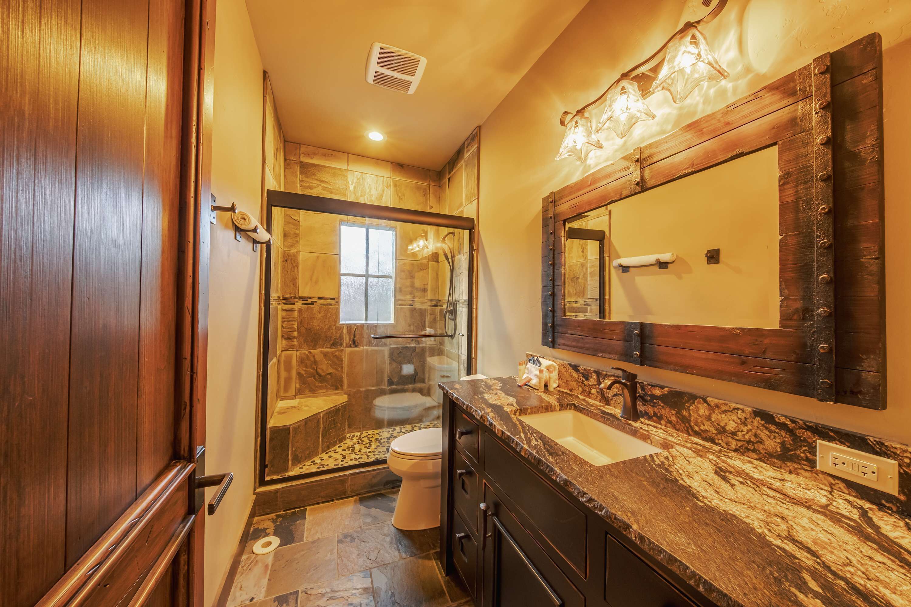A bathroom with a marble countertop, a large mirror, and a shower area.