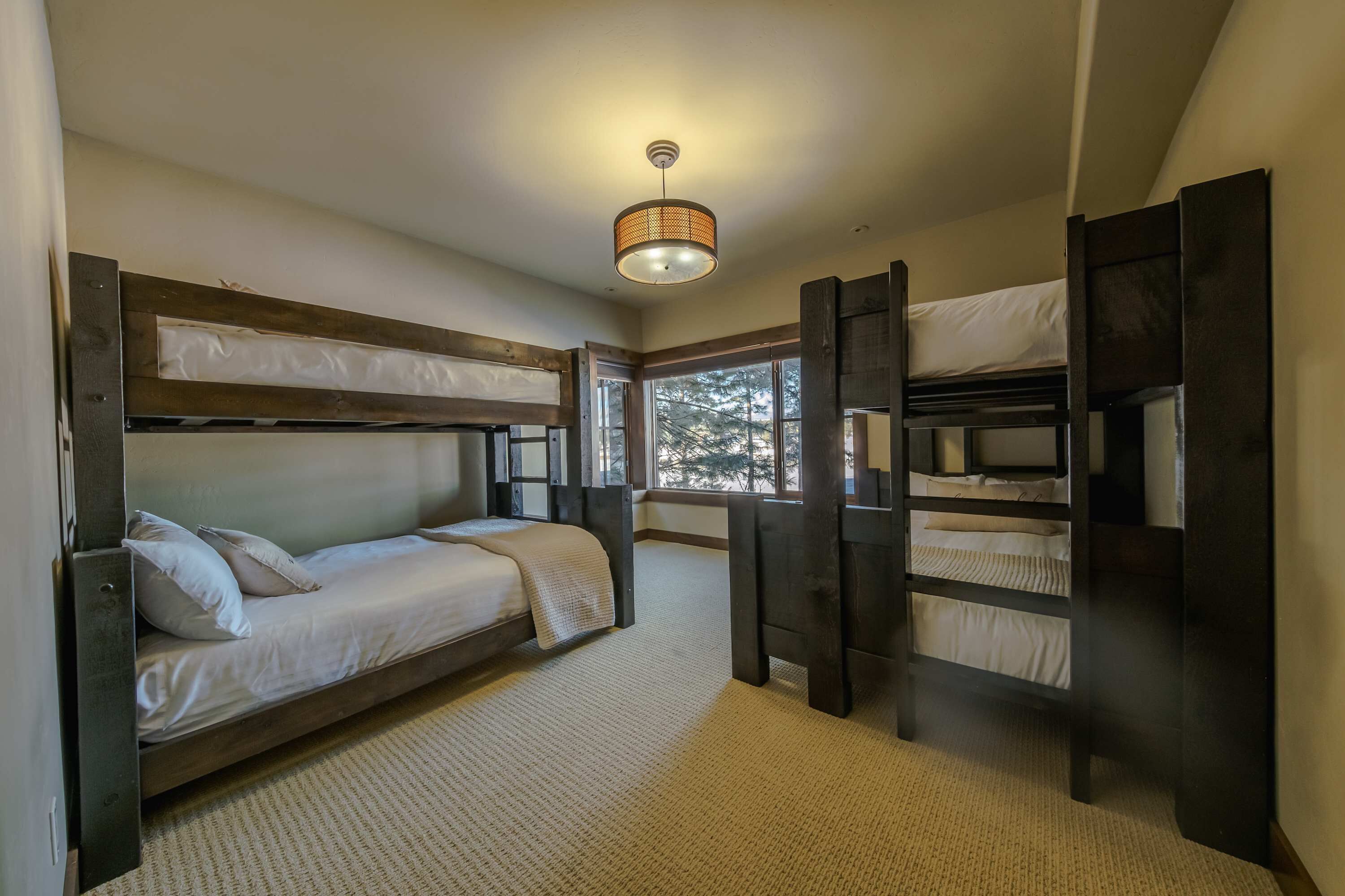Een slaapkamer met stapelbed, uitzicht door het raam, een plafondlamp en een vloerbedekking.
