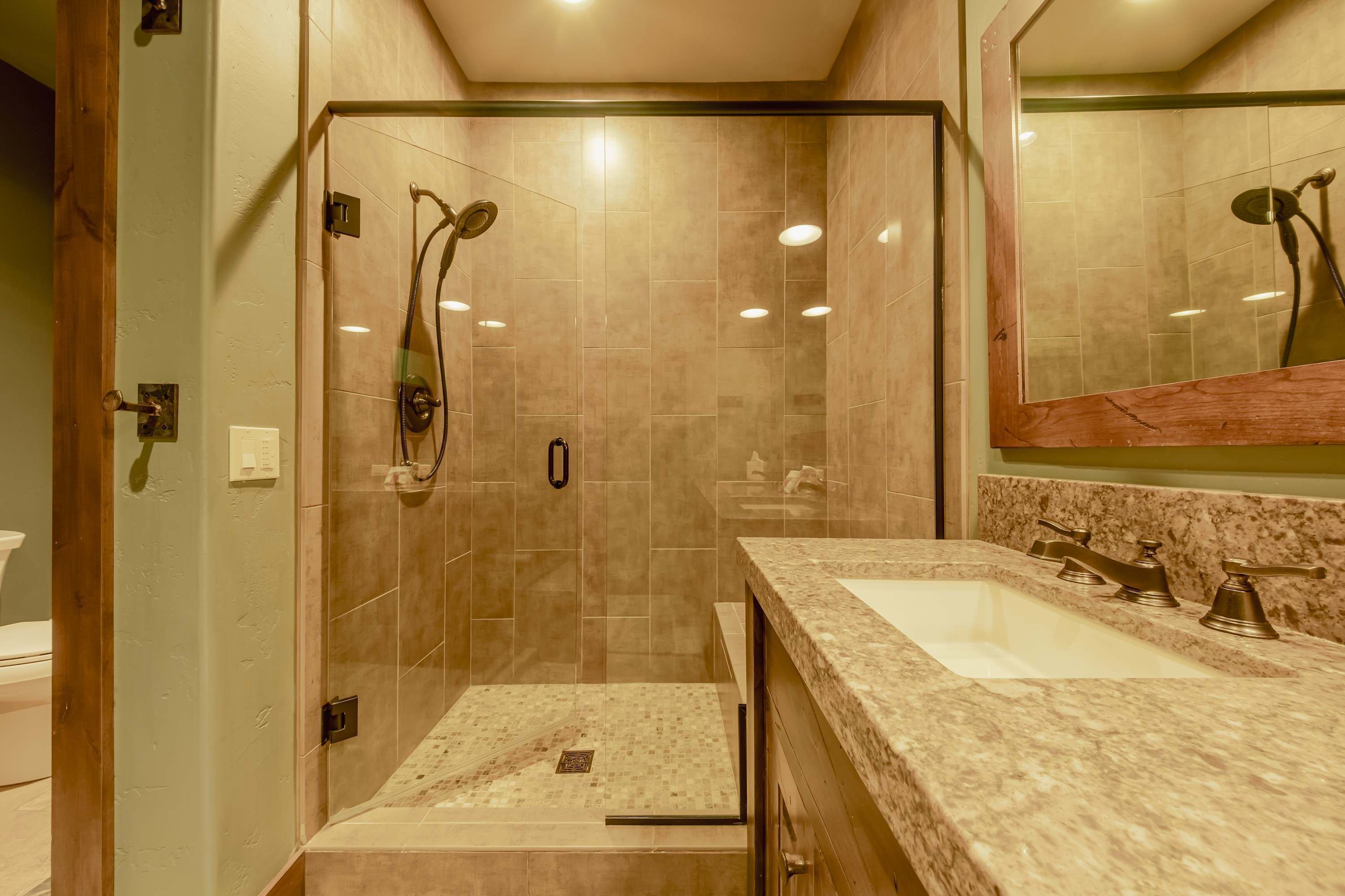 A modern bathroom with a glass-enclosed shower, two sinks with marble countertops, and a large mirror above the sink.