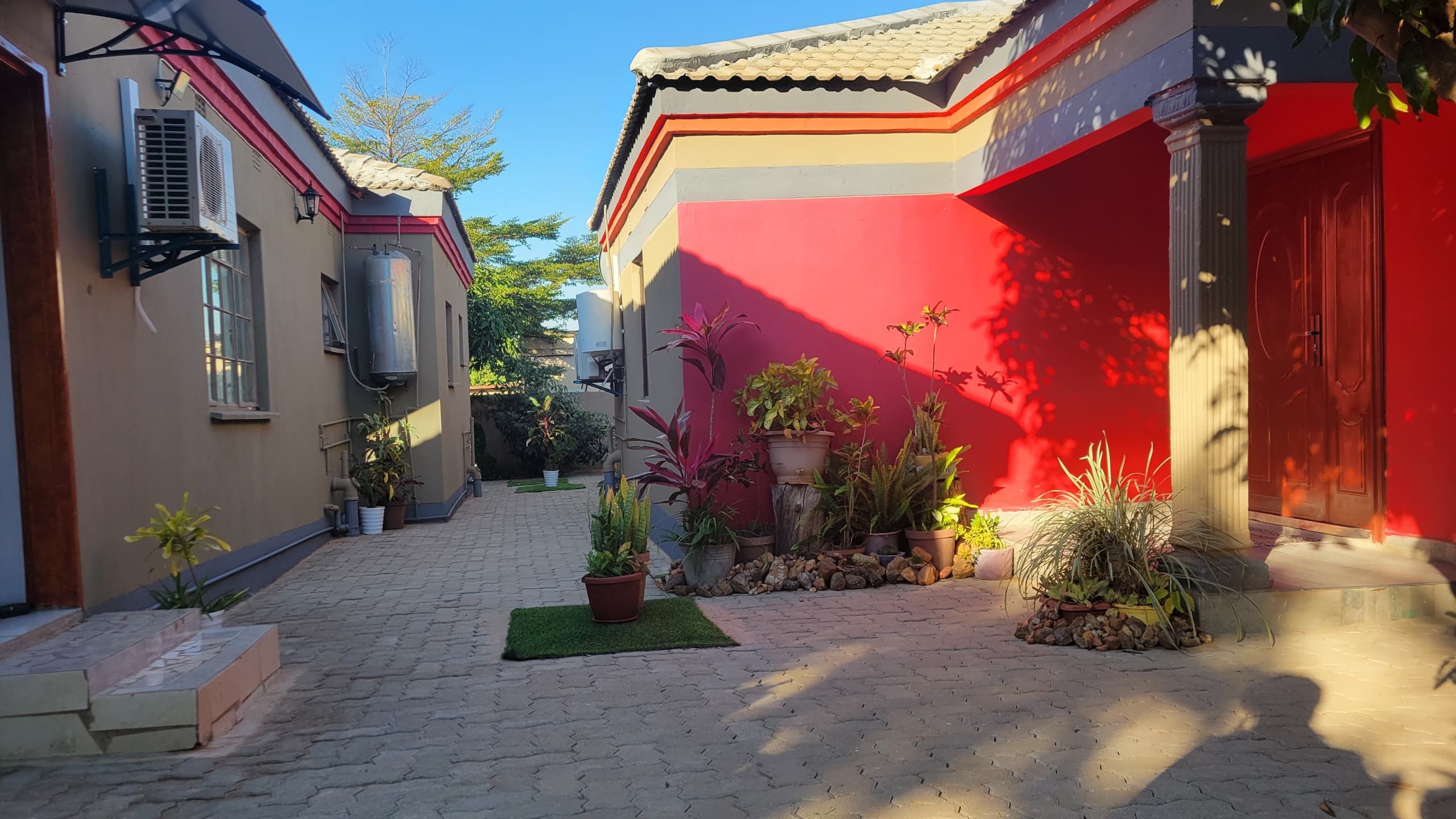 Um pátio com calçada de pedra, plantas em vasos e um edifício vermelho com telhado de telhas.