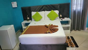 A hotel room with a bed, bedside tables, a small refrigerator, and a window with curtains.