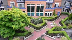 Ein angelegter Innenhof mit geometrisch gestalteten Blumenbeeten, umgeben von mehrstöckigen Gebäuden mit Balkonen.
