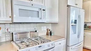 Una cocina con muebles blancos, un microondas empotrado, una estufa a gas y un refrigerador.