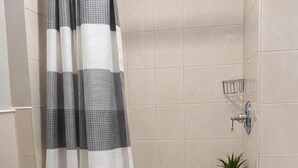 A bathroom with a shower curtain, a toilet, a small stool with a plant, and a tiled wall. - Discover the Comfort of Columbia University Area-1 (New York)