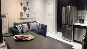 A modern kitchen with a stainless steel refrigerator, a coffee maker, and a dining area with a table and a sofa. - Discover the Comfort of Columbia University Area-1 (New York)