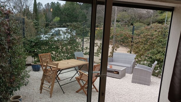 Een terras met een tafel en stoelen, omringd door potplanten en een grindpad.