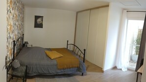 Een slaapkamer met een bed, nachtkastje, lamp, raam met gordijnen en een deur naar een balkon.