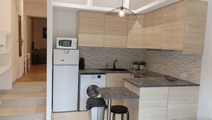 Een moderne keuken met een ingebouwde wasmachine, een magnetron en een spoelbak. Er staan twee krukken en een prullenbak.