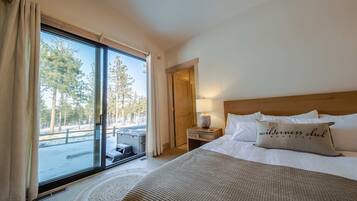 A hotel room with a large window, a bed with a 'wilderness club' pillow, a bedside table with a lamp, and a view of a snowy outdoor area.