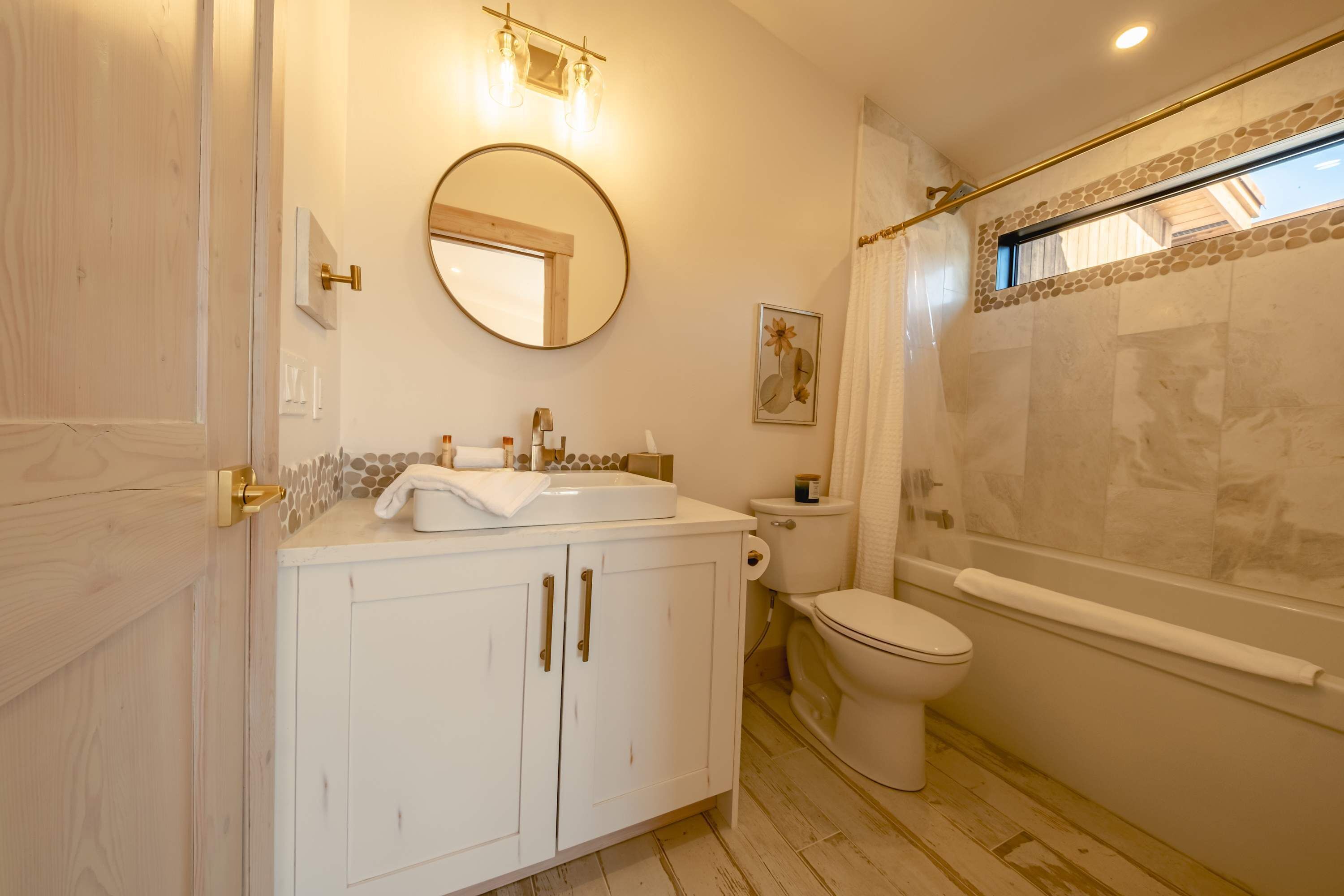 A bathroom with a white vanity, a round mirror, a toilet, and a bathtub.
