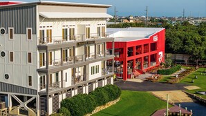 A multi-story hotel with a red and white facade, outdoor seating area, and a view of the surrounding neighborhood. - 2-Bedroom, 1.5-Bathroom Suite at REAL Watersports (Waves)
