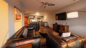 A living room with a sofa, ottoman, and a TV mounted on the wall. - 2-Bedroom, 1.5-Bathroom Suite at REAL Watersports (Waves)