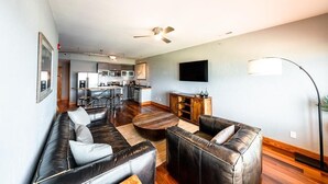 A modern living room with leather sofas, a wooden coffee table, and a kitchen in the background. - Waterfront 2-Bedroom, 1.5-Bathroom Suite at REAL Watersports (Waves)