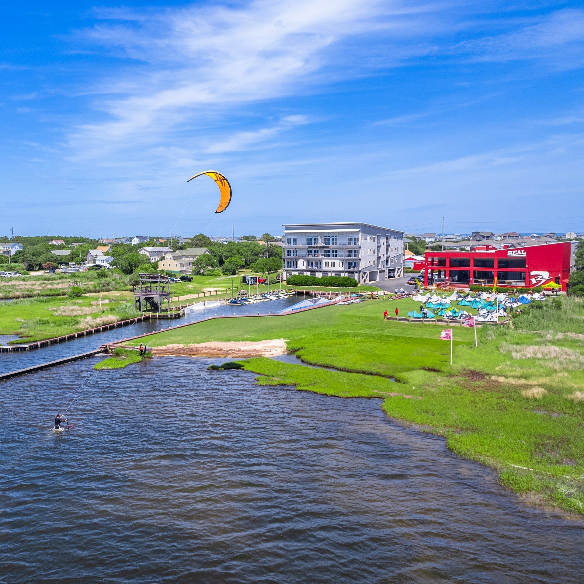 A riverside view with a building, a red structure, and a person windsurfing.
