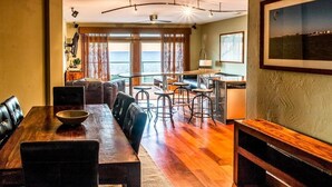 A dining area with a long wooden table, black chairs, and a bar area with stools. - Waterfront 3-Bedroom, 2.5-Bathroom Penthouse Suite at REAL Watersports (Waves)