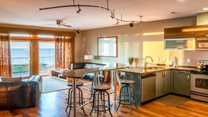 A modern kitchen with a central island, bar stools, and a view of the ocean. - Waterfront 3-Bedroom, 2.5-Bathroom Penthouse Suite at REAL Watersports (Waves)