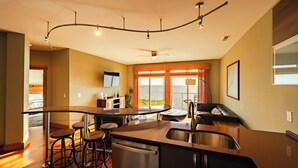 A modern kitchen with a central island, bar stools, a built-in dishwasher, and a large window with a view of the sea. - Waterfront 3-Bedroom, 2.5-Bathroom Penthouse Suite at REAL Watersports (Waves)