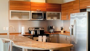 A modern kitchen with wooden cabinets, stainless steel appliances, a marble countertop, and a coffee maker. - Waterfront 3-Bedroom, 2.5-Bathroom Penthouse Suite at REAL Watersports (Waves)