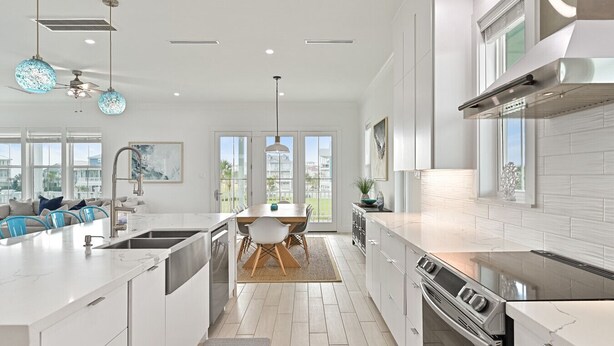 Una cocina moderna con armarios blancos, una isla central y un comedor con vistas al exterior.