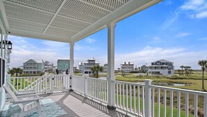 Un espacio exterior techado con piscina, barandillas blancas y vista a casas frente al mar.