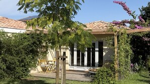 Una casa con portico coperto, terrazza in legno e giardino con diverse piante e una pergola.