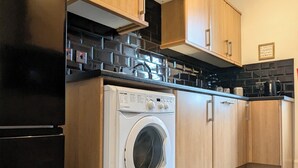 Eine moderne Küche mit Holzausstattung, einer integrierten Waschmaschine und einem schwarzen Kühlschrank.