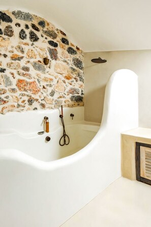A modern bathroom with a stone wall, a white bathtub, and a wooden cabinet. - Villa Castelli - Five Bedroom Villa, Sleeps 10 (Pirgos Kallistis)