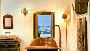 Une salle de bain avec une baignoire, un miroir, un lavabo et une fenêtre donnant sur un paysage enneigé.