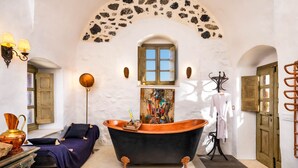 Une salle de bain avec une baignoire sur pieds, une porte en bois, un porte-serviettes et une arche en pierre au-dessus de la fenêtre.