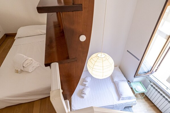 Habitación de hotel con cama, una silla de madera, lámpara colgante y ventana con vistas.