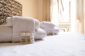 Un letto rifatto con asciugamani bianchi piegati e due flaconi di prodotti per la cura dei capelli.