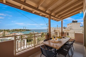 A balcony with a wooden table and chairs, overlooking a coastal view with buildings and a clear sky. - Verkon Villas Seaview Senses (Malevizi)