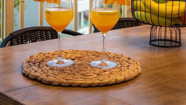 Zwei Gläser Orangensaft auf einer gewebten Unterlage, mit Blick auf das Meer.