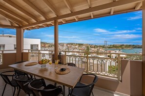 A balcony with a wooden table and chairs, overlooking a coastal town. - Verkon Villas Seaview Senses (Malevizi)