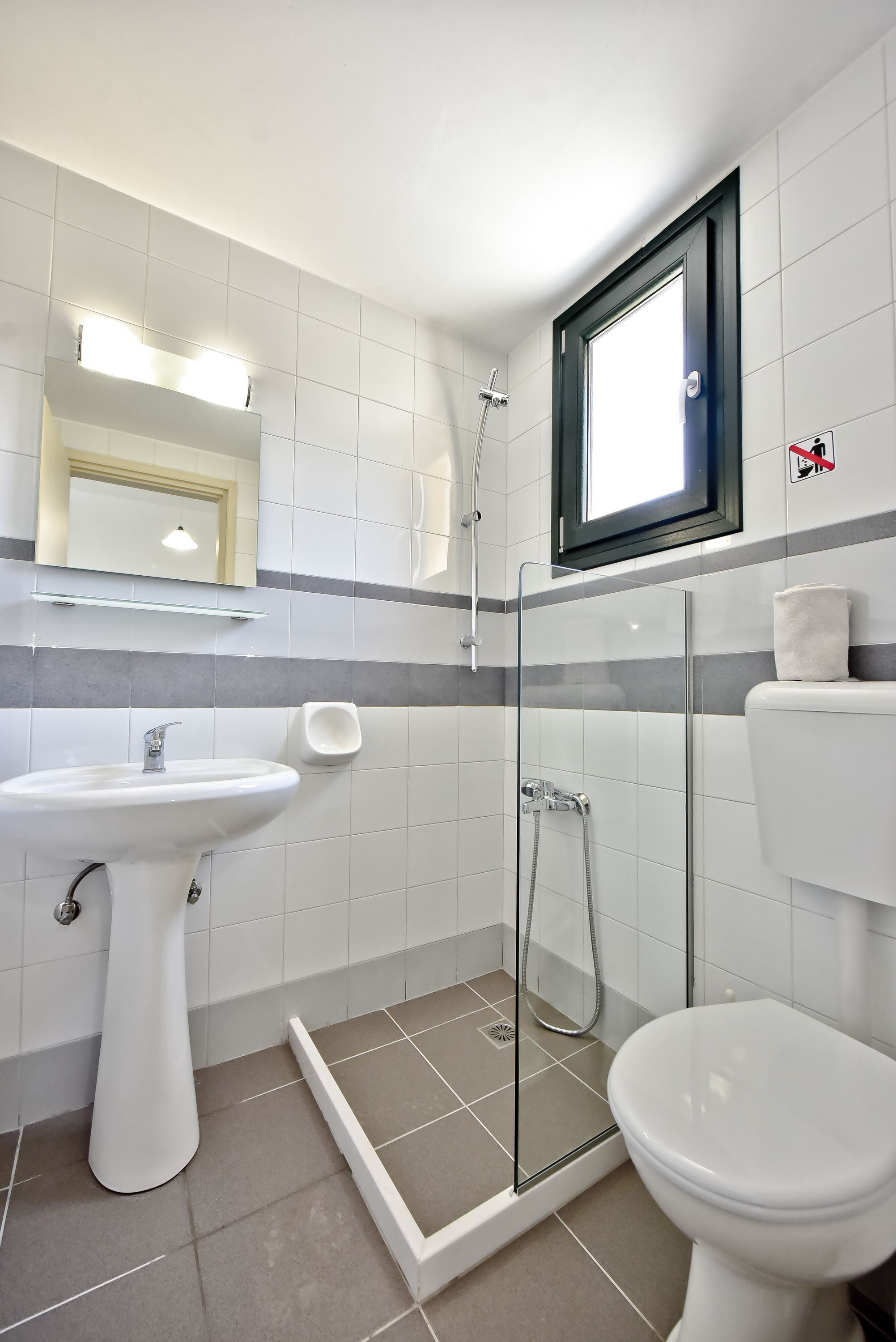 Moderni kylpyhuone, jossa on lasiseinällä varustettu suihku, jalkapallin muotoinen pesuallas ja wc.