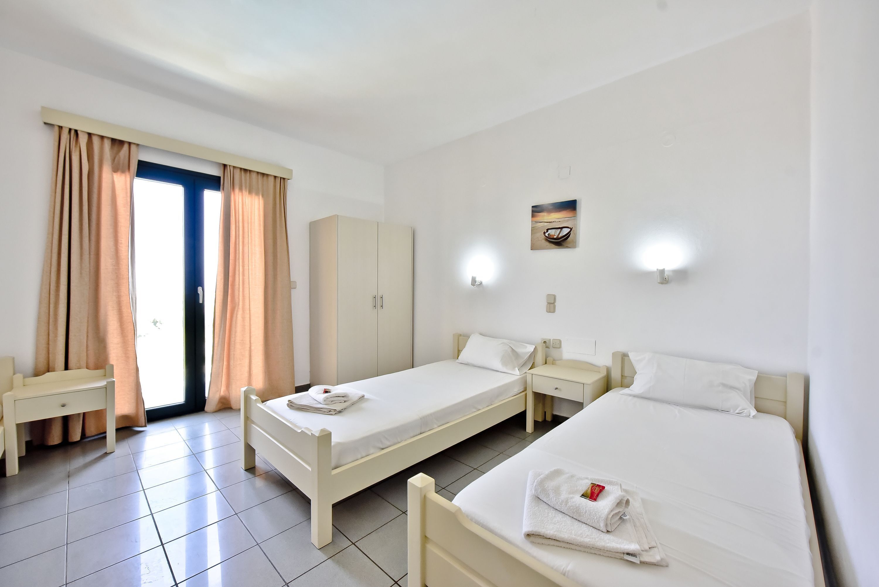 Quarto de hotel com duas camas de solteiro, uma escrivaninha, um guarda-roupa e uma porta de correr de vidro.