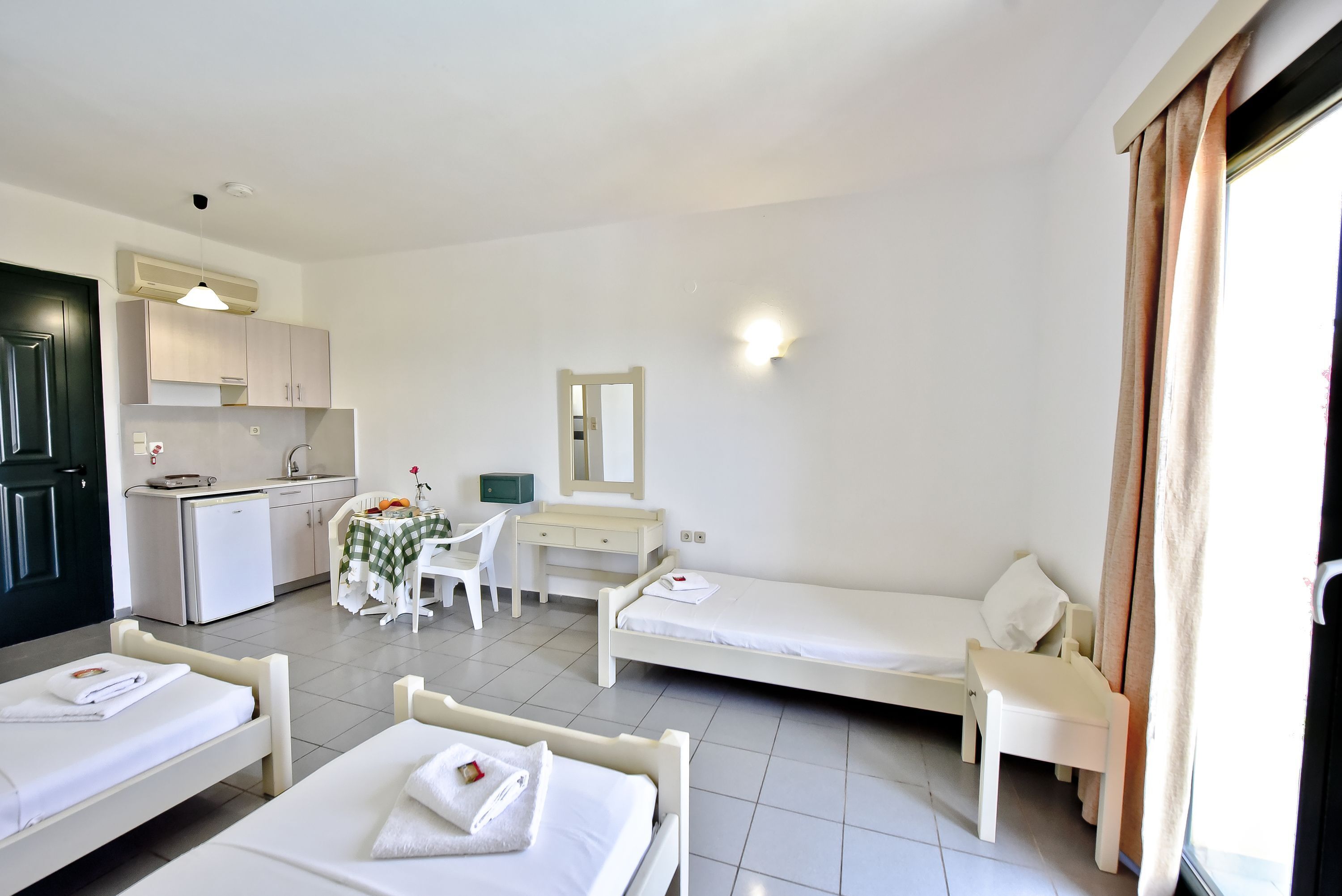A hotel room with two single beds, a desk with a chair, a small kitchenette, and a bathroom.