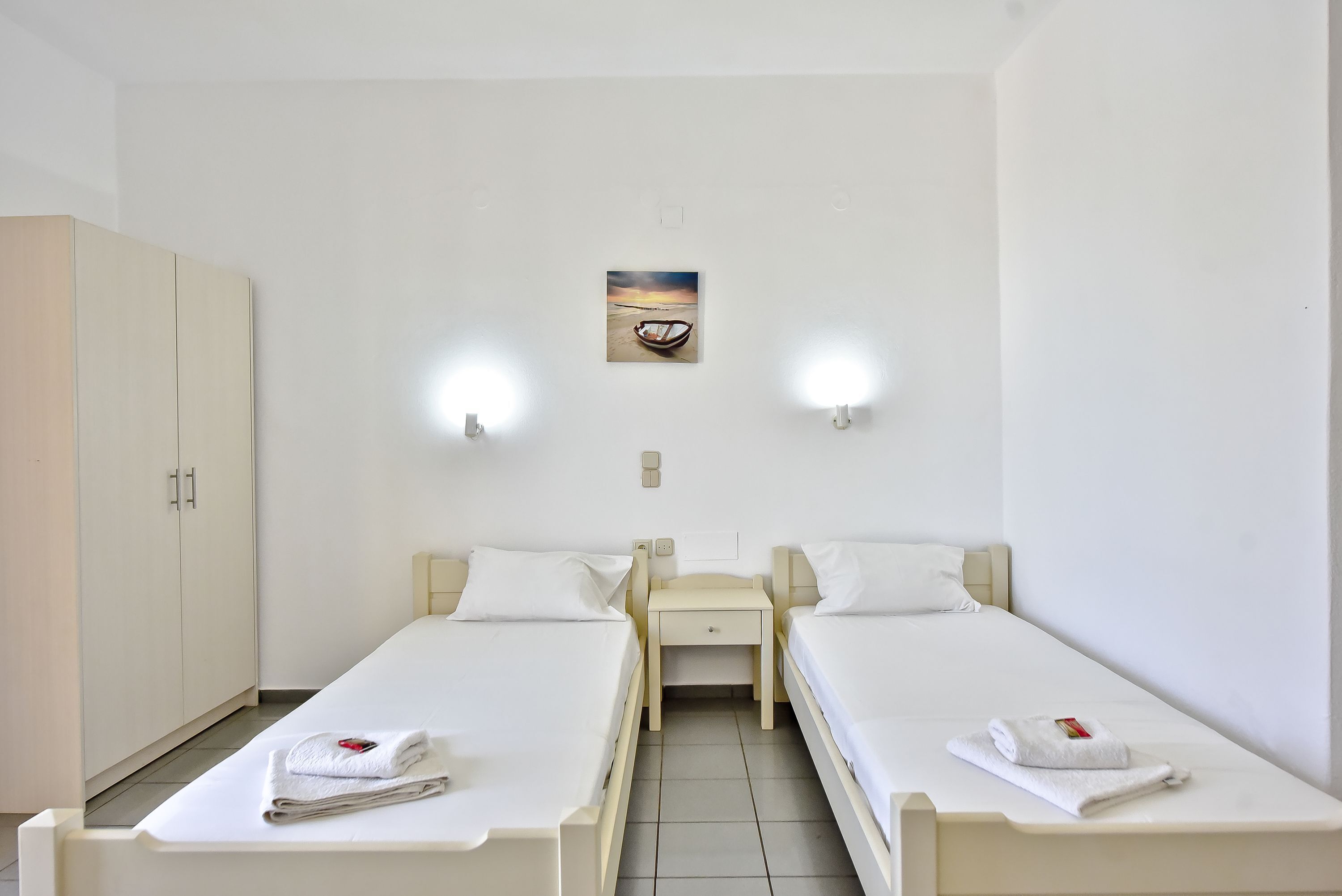 A twin room with two single beds, a small bedside table with a phone, a cabinet, and a painting on the wall.