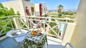 Un balcón con una mesa dispuesta para dos, una silla y vistas al mar y a la vegetación.