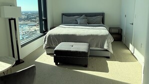 A modern hotel room with a large bed, a small table, and a view of the city through a large window. - Stylish King Suite • Tysons Corner Mall Access • Metro Nearby (Tysons)