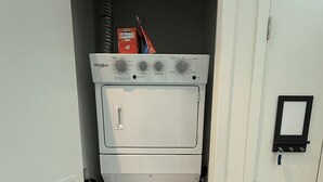 A compact laundry room with a front-loading washer and dryer, a small storage cabinet, and a door with a key lock. - Stylish King Suite • Tysons Corner Mall Access • Metro Nearby (Tysons)