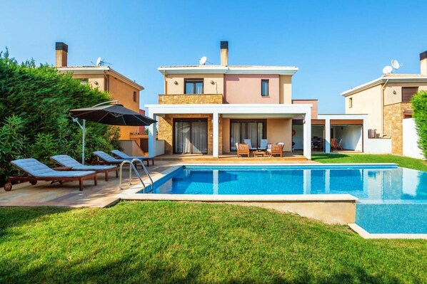 A modern two-story house with a swimming pool, outdoor seating, and a well-maintained lawn.