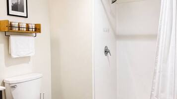A bathroom with a toilet, shower, and a towel rack with a picture above it.