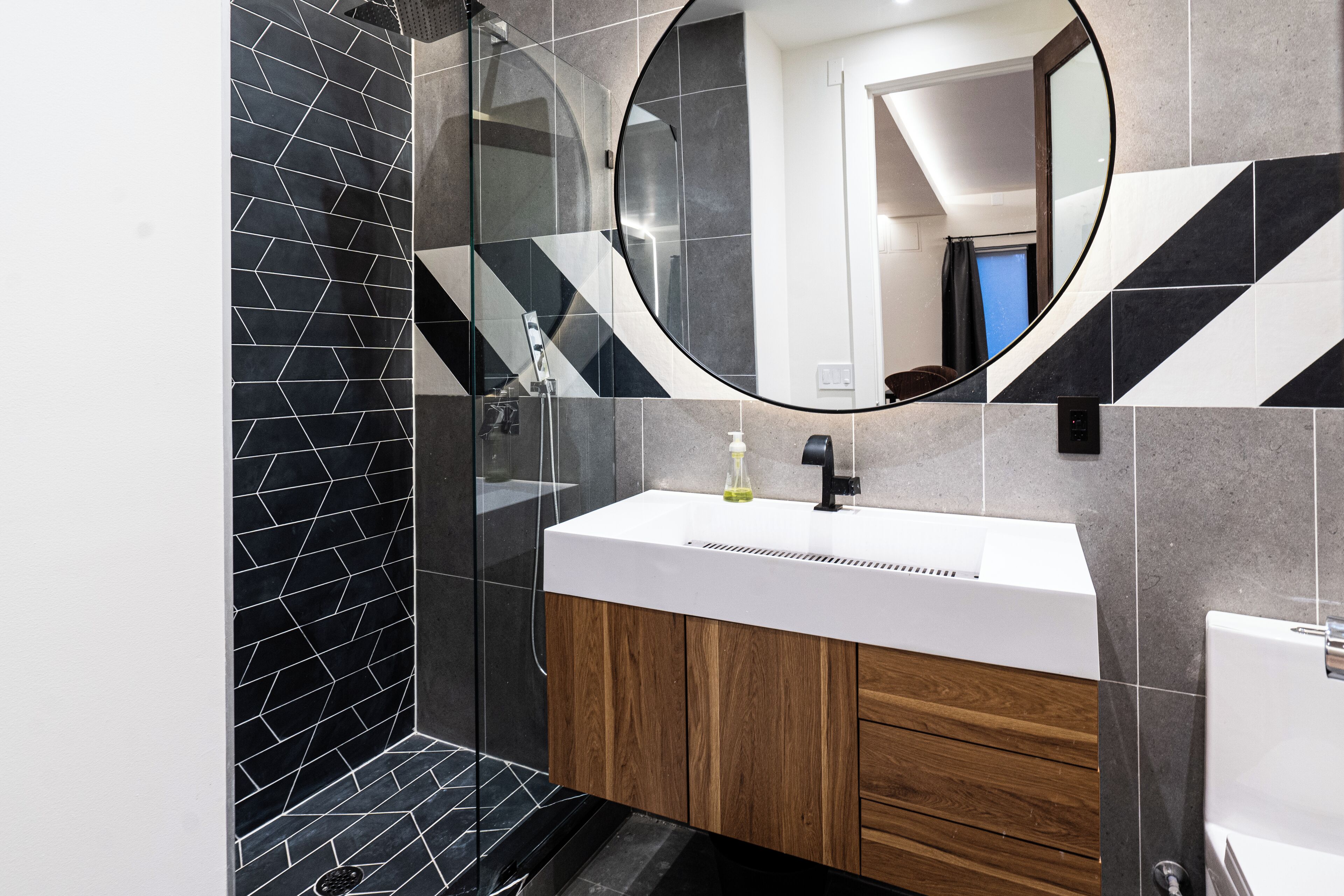 A modern bathroom with a glass shower enclosure, a white sink, and wooden cabinets.