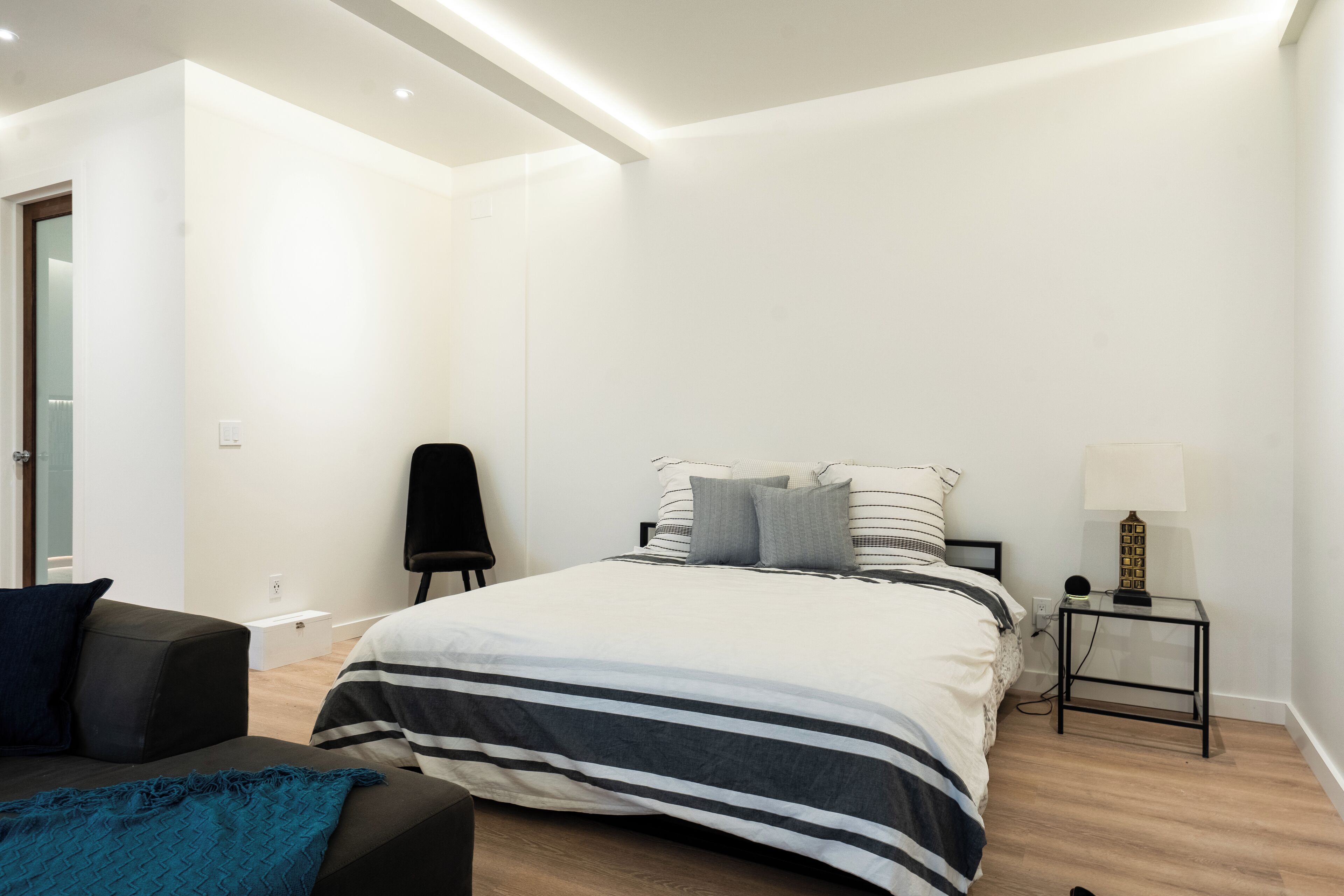 Un dormitorio moderno con una cama grande, una mesita de noche con lámpara, una silla y una pequeña mesa.