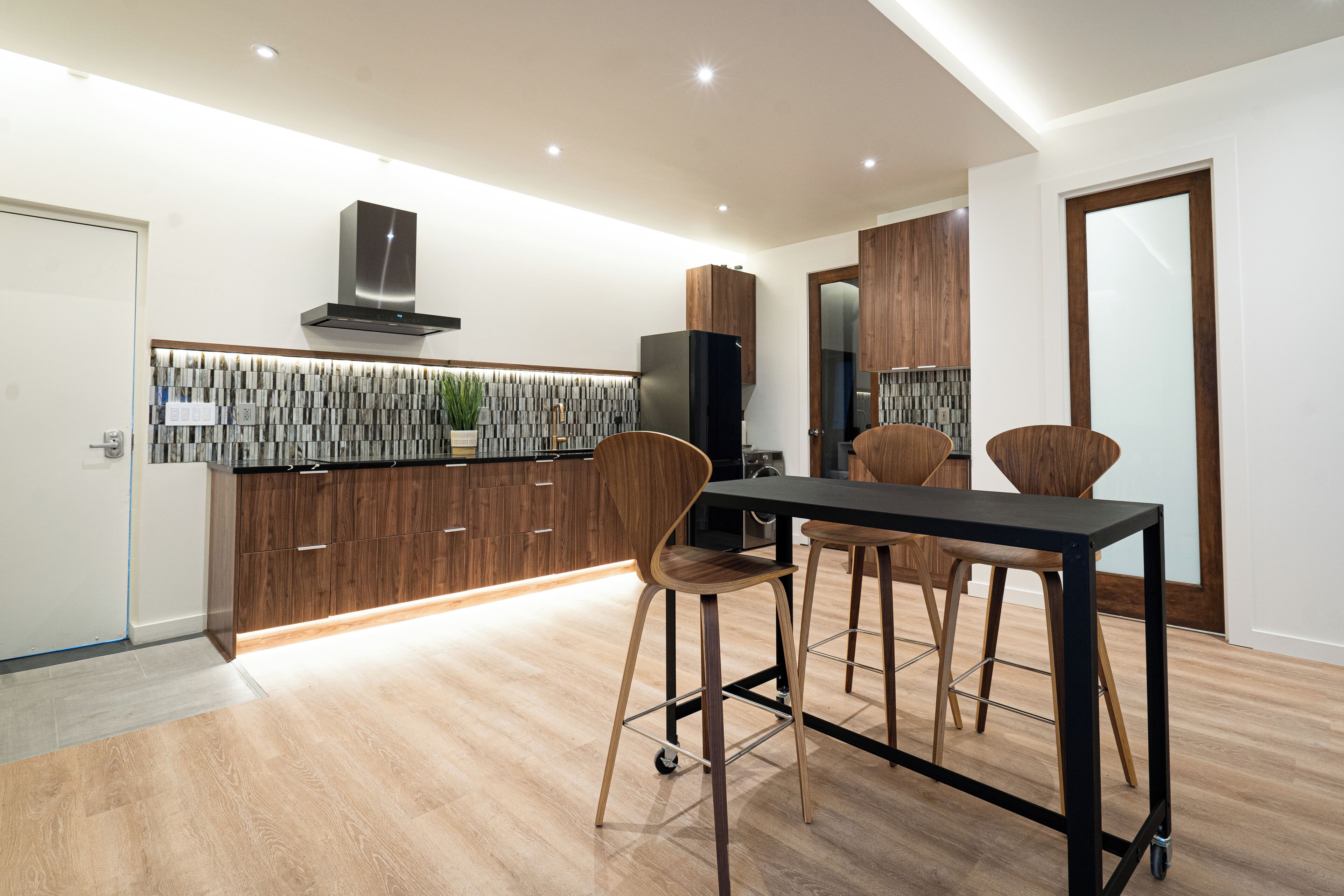 A modern kitchen with wooden cabinets, a black countertop, and a dining area with stools.