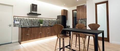 A modern kitchen with wooden cabinets, a black countertop, and a dining area with stools.
